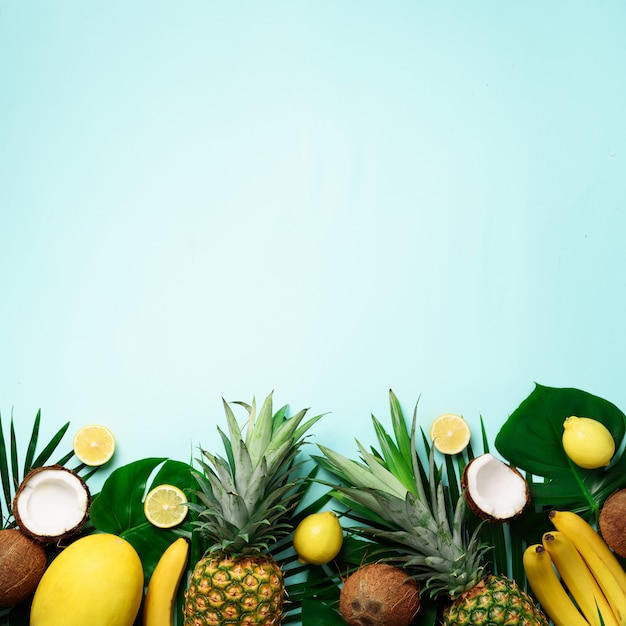Exotische ananas, rijpe kokosnoten, banaan, meloen, citroen, tropische palm en monsterabladeren op blauwe achtergrond