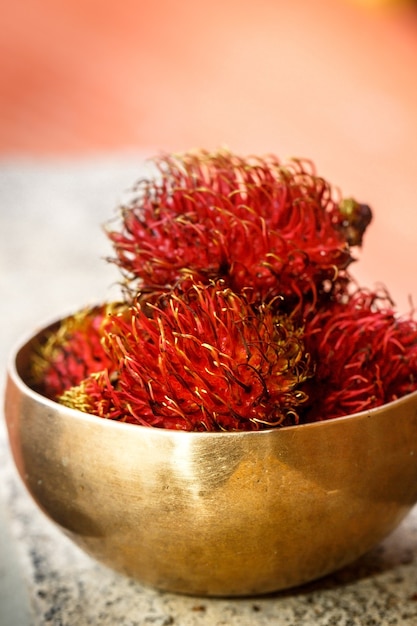 Exotische harige fruitramboetan in vintage gouden kom op onscherpe achtergrond