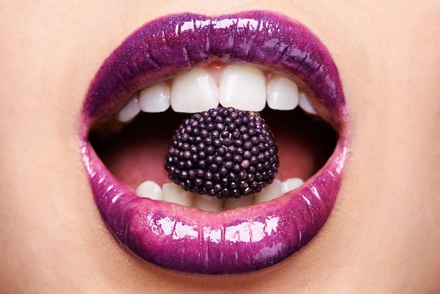 Exotische lekkernijen Shot van een vrouw die paarse lippenstift draagt en in een paars snoepje bijt