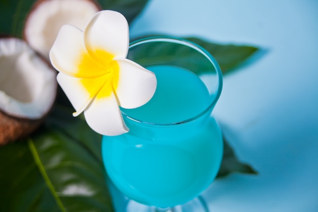 Exotische tropische blauwe Curacao cocktaildrank in een glas met Plumeria-frangipanibloem, palmblad, verse kokosnoot op de achtergrond.