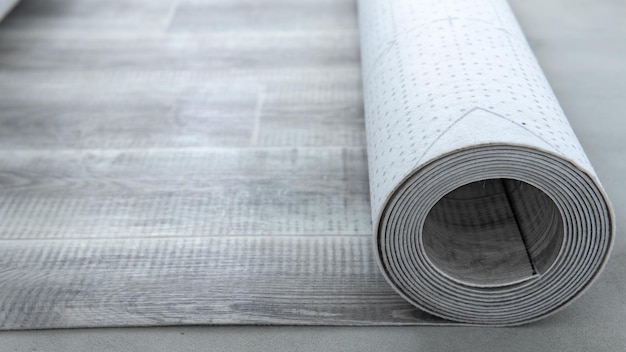 An expanded roll of gray linoleum lies on the concrete floor. Construction work at home