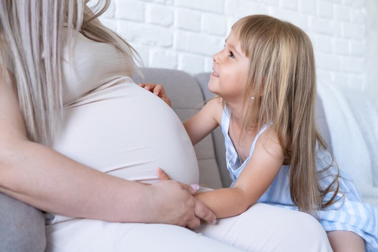 배를 쓰다듬어 작은 아기 딸과 함께 침대에 앉아 기대하는 어머니