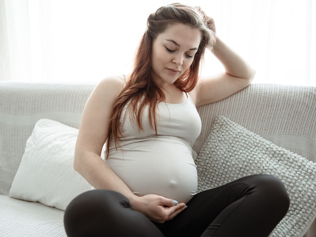 The expectant mother with a big belly is sitting on the couch at home.