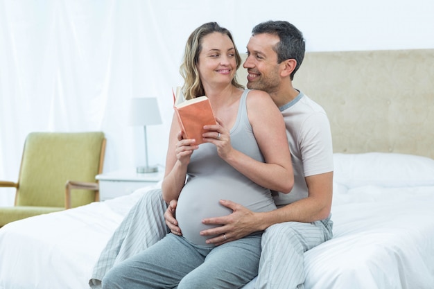 Expecting couple sitting on bed and reading book