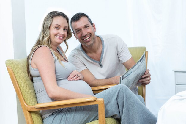 Expecting couple sitting on chair and reading news paper