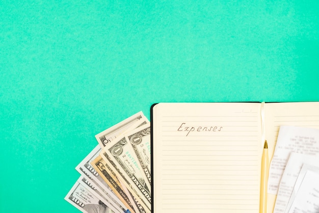 Expenses accounting concept. Directly above view of dollar banknotes, receipts, pen and notepad with handwritten words Expenses on green background, copy space