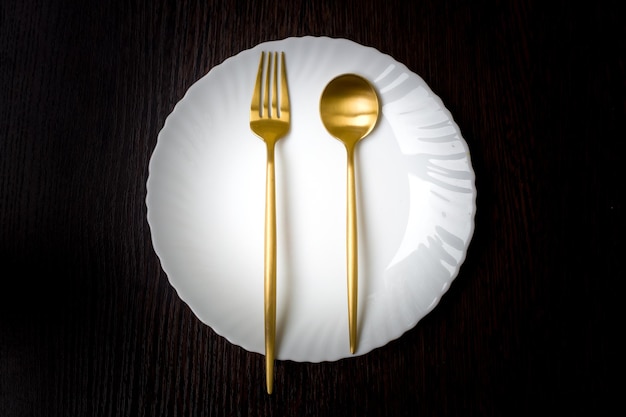 Expensive cutlery on a white plate, golden spoon, gold fork