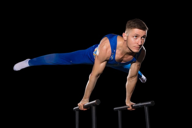 Experience. Muscular male gymnast training in gym, flexible and active. Caucasian fit guy, athlete in blue sportswear doing exercises for strength, balance. Movement, action, motion, dynamic concept.