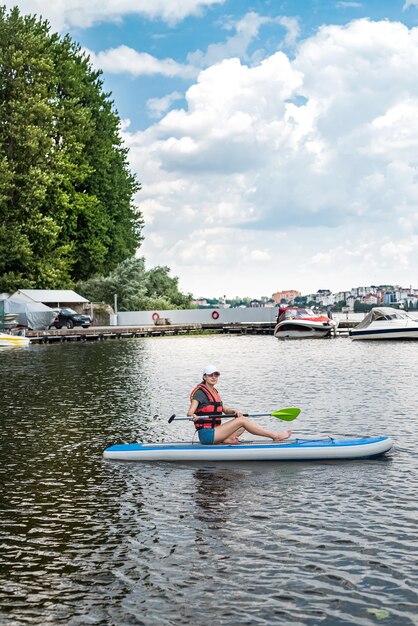 An experienced athlete in a vest rides on the water on a board sap on the lake in weather