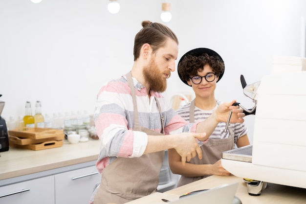 Experienced barista teaching new employee to use espresso machin