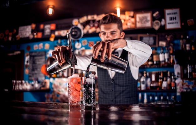 Photo experienced barkeeper mixes a cocktail while standing near the bar counter in bar