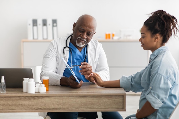 Photo experienced black doctor explaining treatment plan to female patient