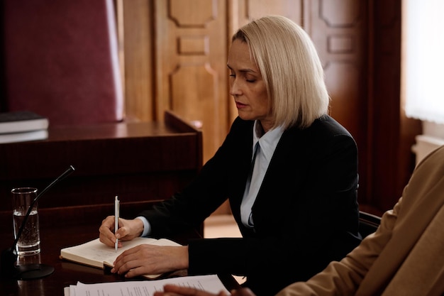 Experienced blond female jury or prosecutor making notes in notebook