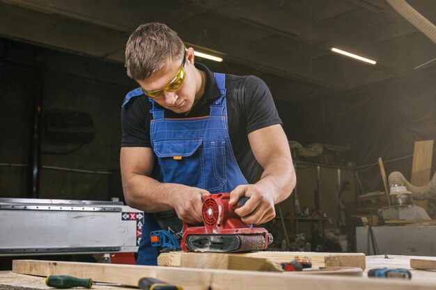 Photo experienced carpenter in work clothes and small buiness owner working in woodwork workshop using sandpaper for polishing wooden in workshop