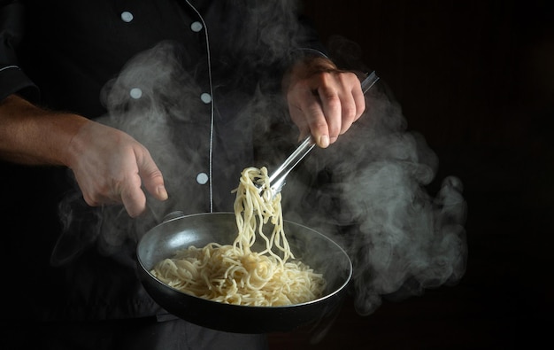 Опытный повар готовит спагетти на горячей сковороде Место для рекламы на черном фоне Итальянская национальная кухня