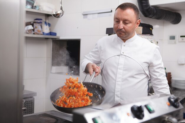 Chef esperto che frigge le verdure nella cucina del ristorante, copia spazio