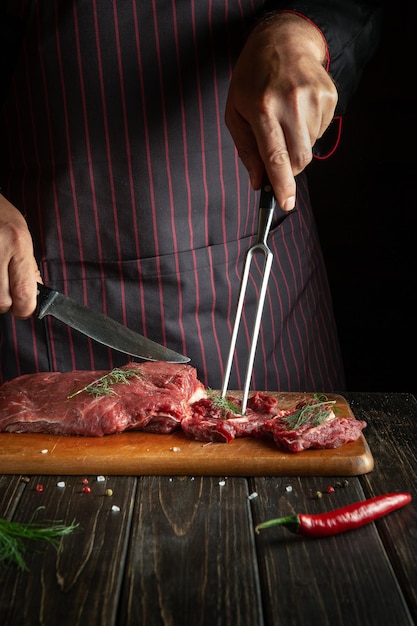 An experienced chef prepares raw fresh beef meat for roasting or barbecue Working environment in the kitchen of a restaurant or hotel