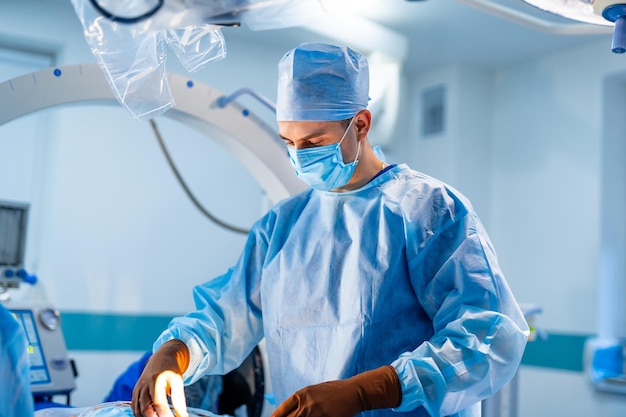 Experienced doctor in surgery room during operation. Medic in blue scrubs in modern clinic interior. Closeup.