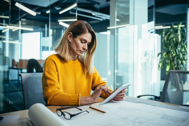 Experienced female architect freelancer works in a modern office on drawings uses a tablet