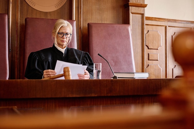 Photo experienced female judge in black gown reading juridical paper documents