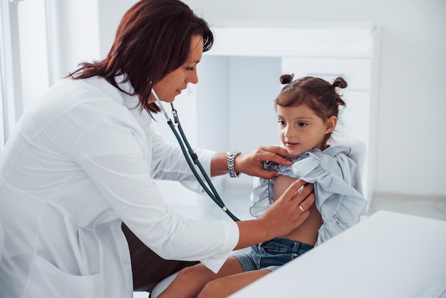 Experienced female pediatrician works with little girl in the clinic.