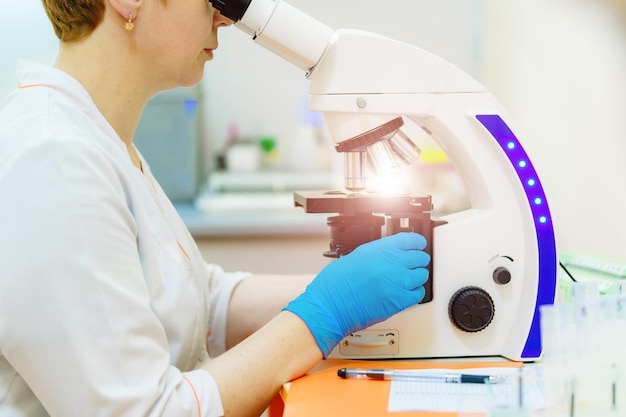 経験豊富な女性科学者が実験室で働いており、顕微鏡で調査を行っています現代の化学実験室の背景側面図