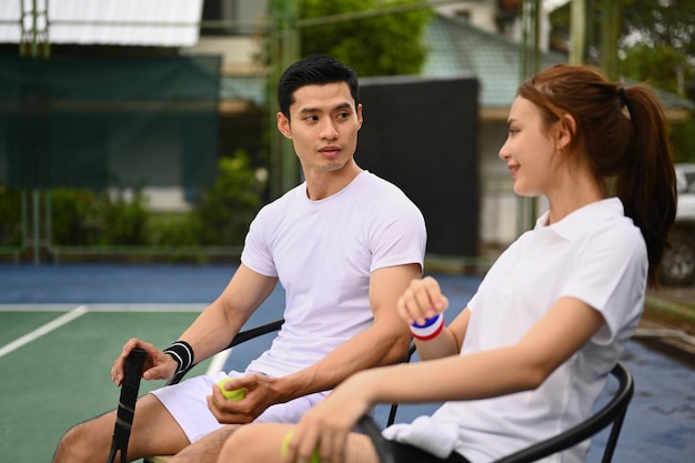 Experienced male tennis coach giving instructions to his student standing by net at the outdoor tennis court