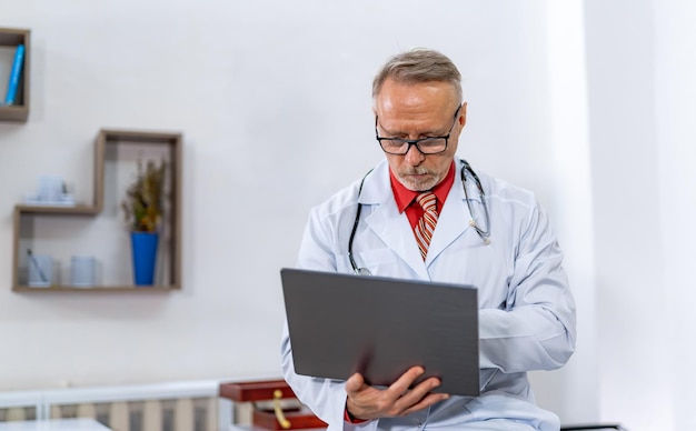 Experienced mature doctor typing on his laptop in bright office Modern clinic Closeup