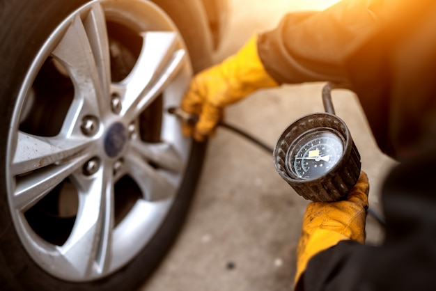 An experienced mechanic in orange gloves is placing air valve on a car wheel preparing to pressurize it.