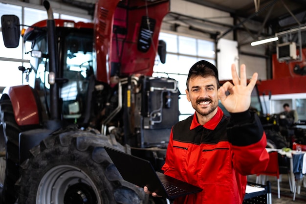 Photo experienced mechanic with diagnostic tool standing by tractor machine inside workshop