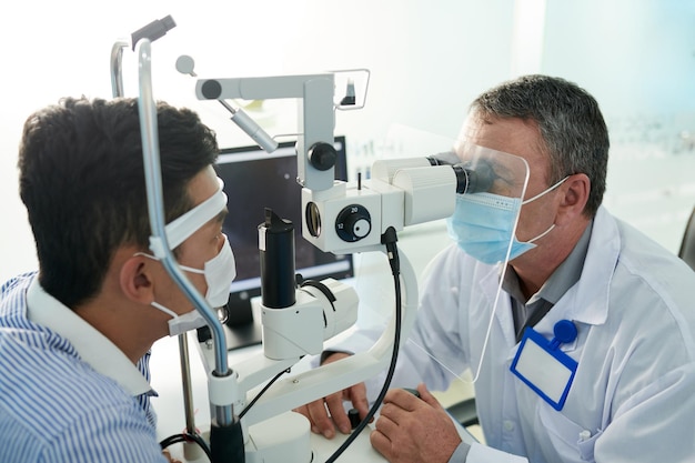 Experienced optometrist testing male patient for glaucoma with modern equipment