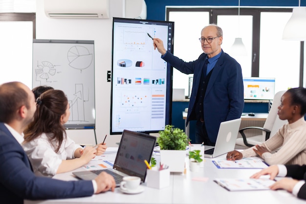 Experienced project leader analysing financial presentation during business conference in brainstorming room using digital devices