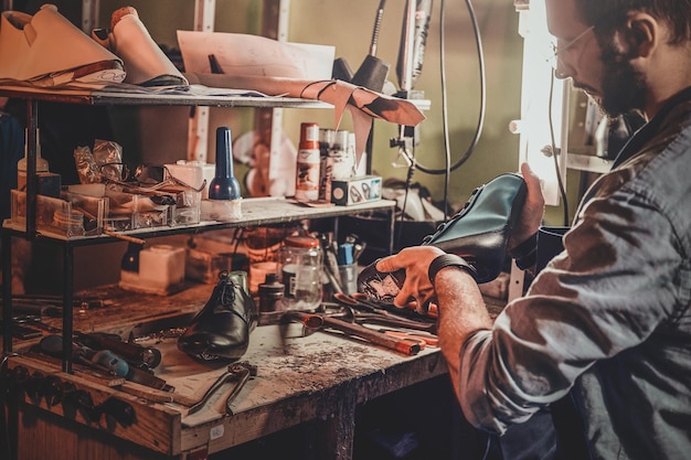 Experienced shoemaker is creating retro leather shoes at his comfortable workshop.