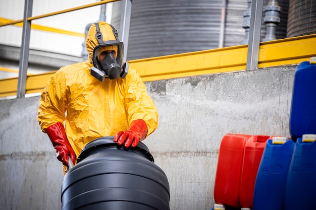 Photo experienced worker in protection suit and gas mask moving barrels with hydrochloric acid