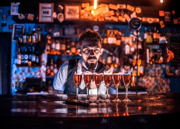 Опытный бармен интенсивно заканчивает свое творение, стоя у барной стойки в ночном клубе