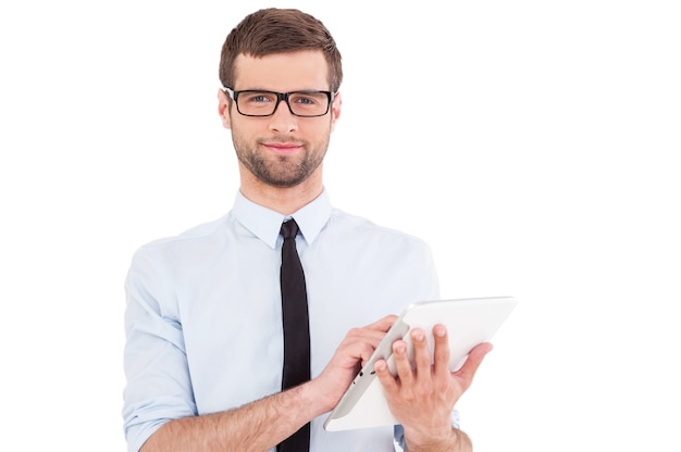 Expert in digital technologies. Cheerful young man in formalwear working on digital tablet and smiling while standing isolated on white background