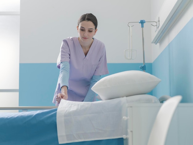 Expert smiling nurse working at the hospital she is making the bed and changing sheets healthcare and medicine concept