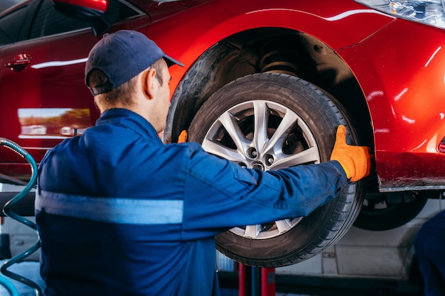 Photo expert specialist technician changes tires tyres of lifted up car at auto service