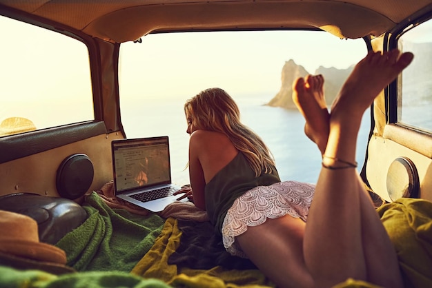 Explore the internet wherever you are Shot of a young woman using her laptop while relaxing in the back of her car on a roadtrip