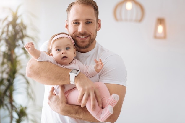 Exploring everything around. Funny cute joyful baby girl lying in hands of the father and looking away while expressing interest and joy