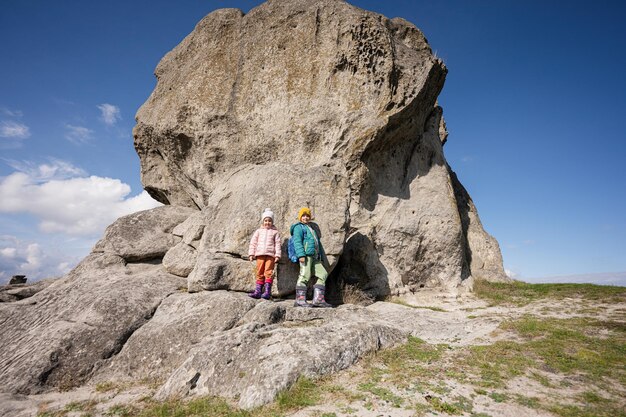 Exploring nature Brother and sister wear backpack hiking near big stone in hill Pidkamin Ukraine