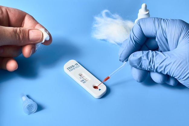 Express COVID-19 test for IgM and IgG antibodies to novel coronavirus SARS-CoV-2, Covid-19. Nurse hand in blue glove applies blood to test. Patient fingers press cotton.