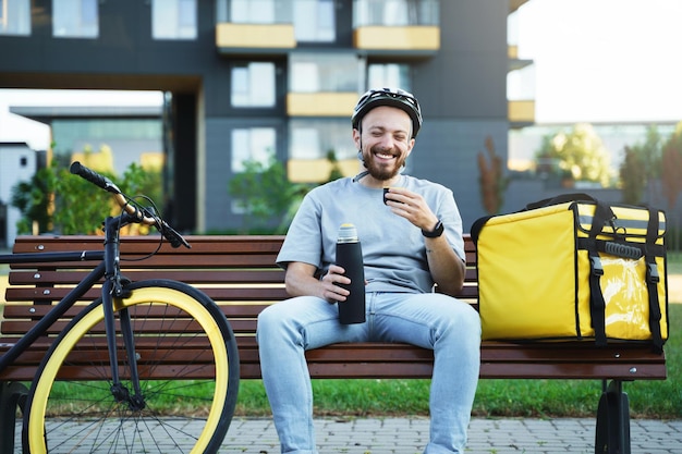 Express delivery courier sitting on bench and drinking coffee