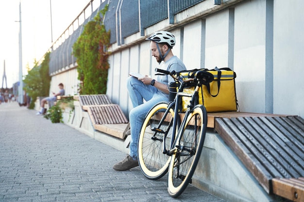 Express delivery courier sitting on bench and reading book