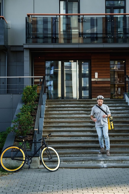 Express delivery courier with insulated bag going down the stairs to his bicycle