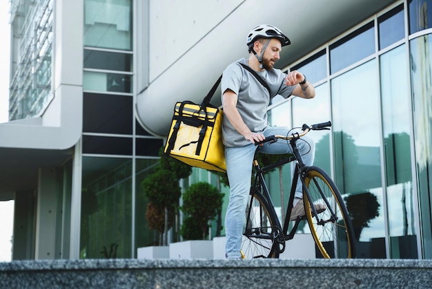 Express koerier met geïsoleerde tas kijken naar horloge op de fiets