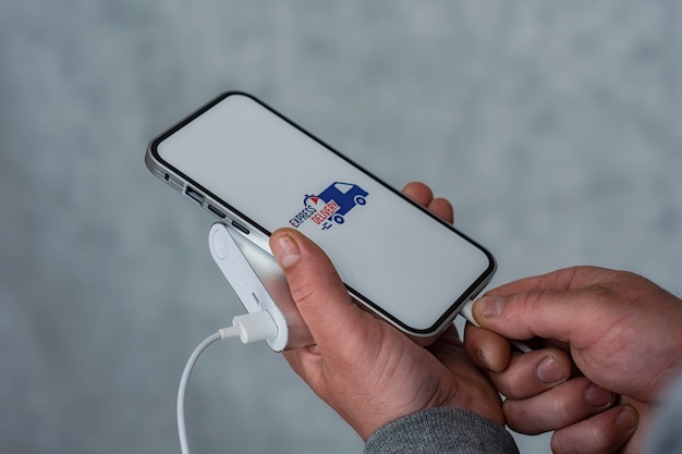 Express levering in uw telefoon. Een man houdt een smartphone met powerbank en pictogram op een wit scherm in zijn handen.