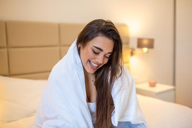 Express tenderness. Cute young woman keeping smile on her face while looking away wrapped at the white blanket. Stock photo