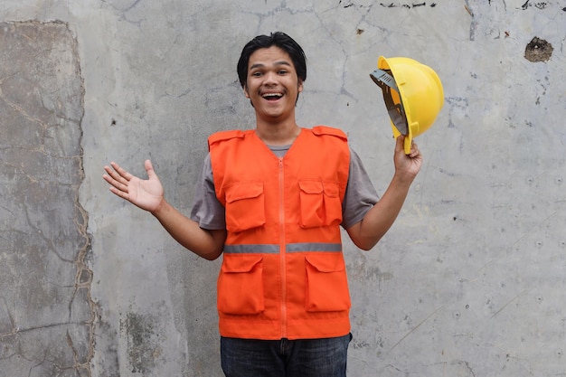 Expressieve aannemer man in vest met helm tegen muur achtergrond