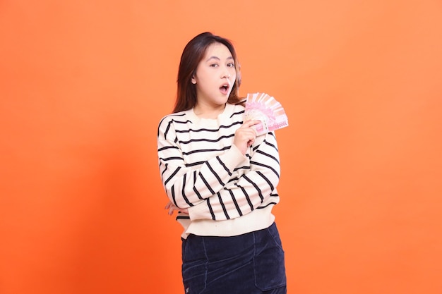 The expression of a shocked Asian woman standing while holding some rupiah money to show off for fas